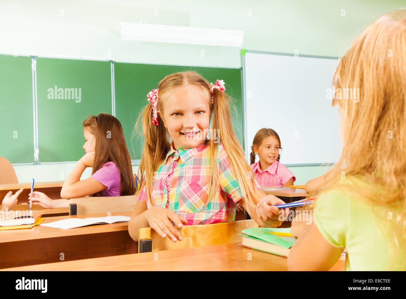Smiling girls turned to classmate giving pencil Stock Photo