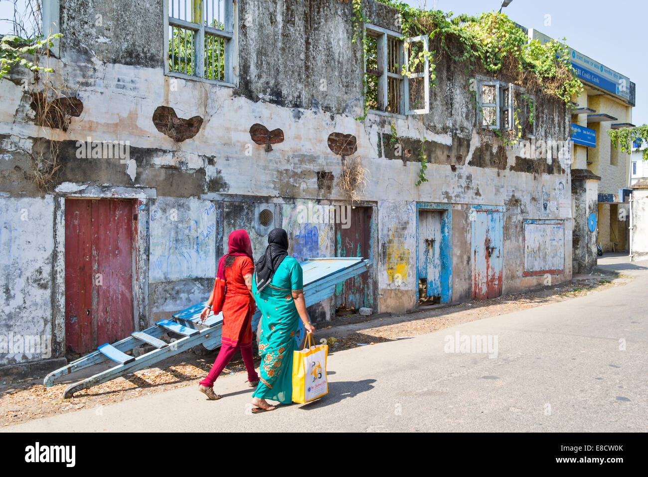 OLD DERELICT BUILDINGS OF PORT KOCHI OR COCHIN INDIA AND PEOPLE IN COLOURFUL DRESS PASSING BY Stock Photo