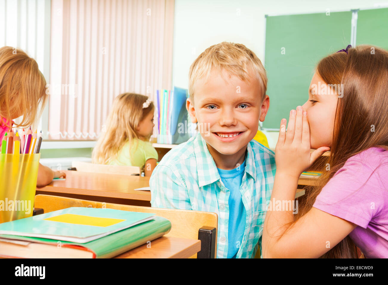 Girl telling secret to smiling boy in classroom Stock Photo