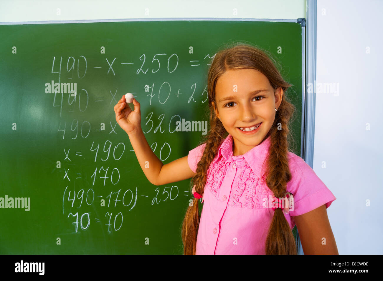 Smiling girl with braids and chalk near blackboard Stock Photo