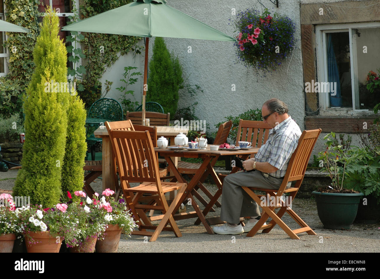 middle aged man sitting at tea table outside cafe in Eyam, Derbyshire Stock Photo