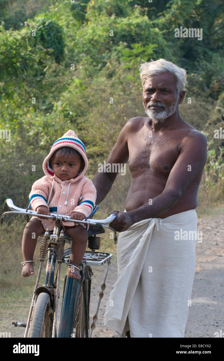 Indian village elder, grandfather, and grandchild astride a bicycle returning to their village near the sacred hill Arunachala Stock Photo
