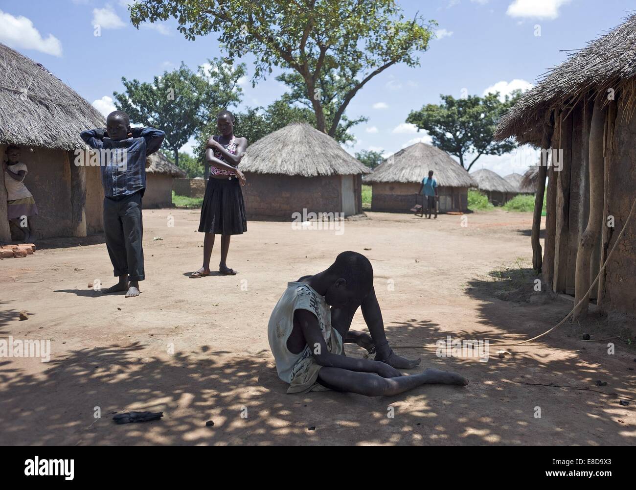 Sept. 13, 2014 - Kampala, Kampala, Uganda - September 13, 2014 - Lapul - Ocwida village (Pader district), Uganda - Nodding Syndrome patient Okot David, 18, sits outside his hut as a younger brother and sister wait for another sibling, so that they can walk to their school district some three hours away. The school season is about to begin so they will stay at the family's other home which is closer to the school. Their brother represents a severe case of Nodding Syndrome; he has been ill with it since 2003. Okot is one of seven children and the only one with the illness. He's tied to his livin Stock Photo