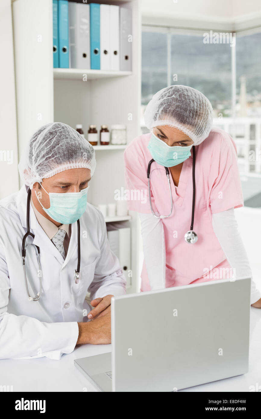Doctors wearing surgical masks while using laptop at medical office