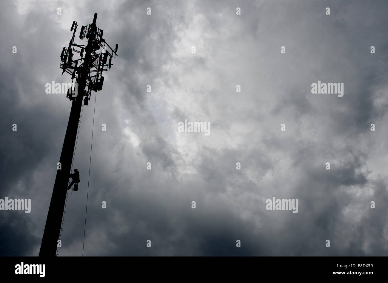 A tower construction worker makes his way down from the top of a Communications Tower to avoid an approaching thunderstorm. Stock Photo