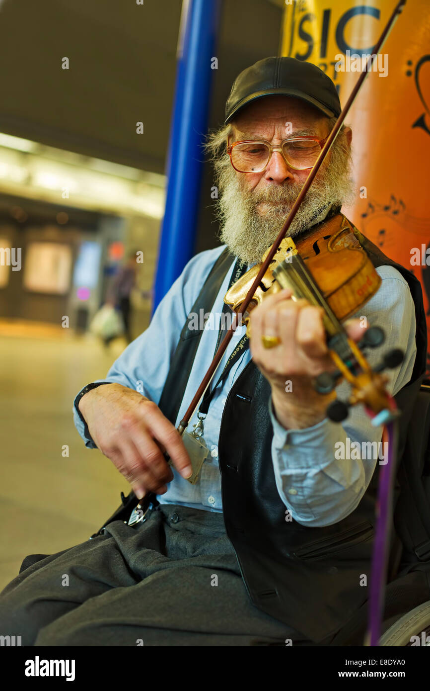 An old busker playing the  violin at a London railway station Stock Photo