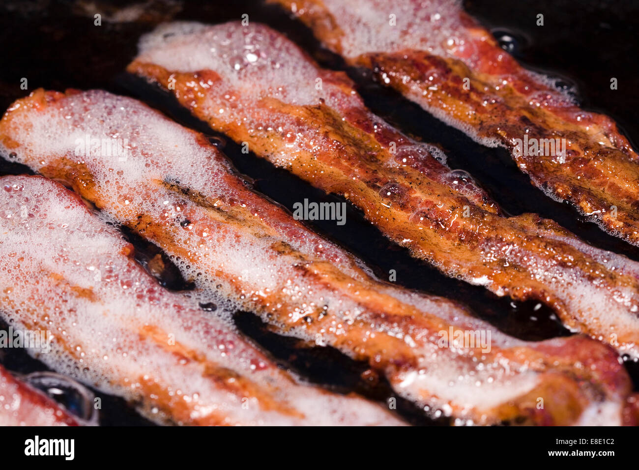 Bacon grease rendering out of strips of streaky bacon in a frying pan