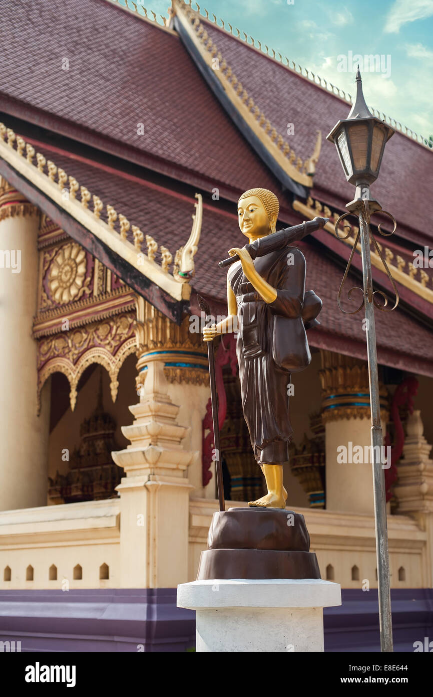 Statue of walking Buddha in traditional theravada style with umbrella and bowl. Asian city religious architecture at public plac Stock Photo