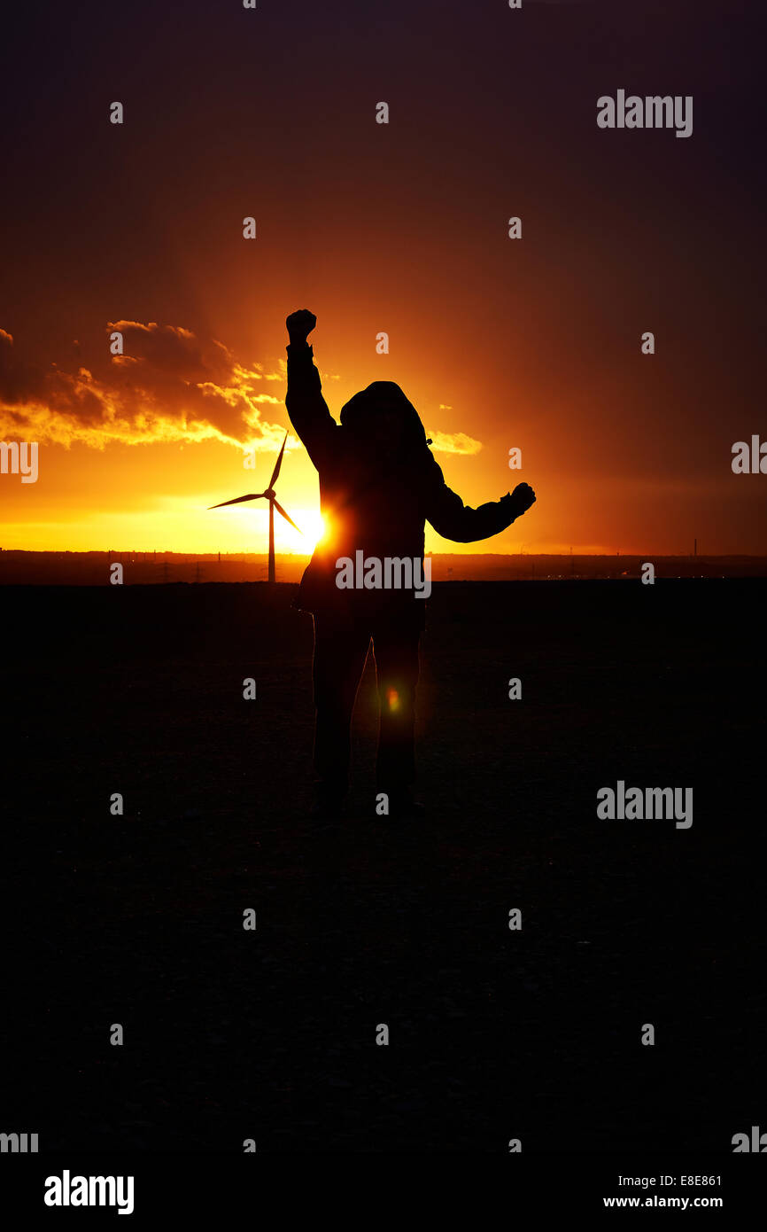 Silhouette of a man holding up his arms in jubilation behind a dark orange colored sunset. Long shot. Stock Photo