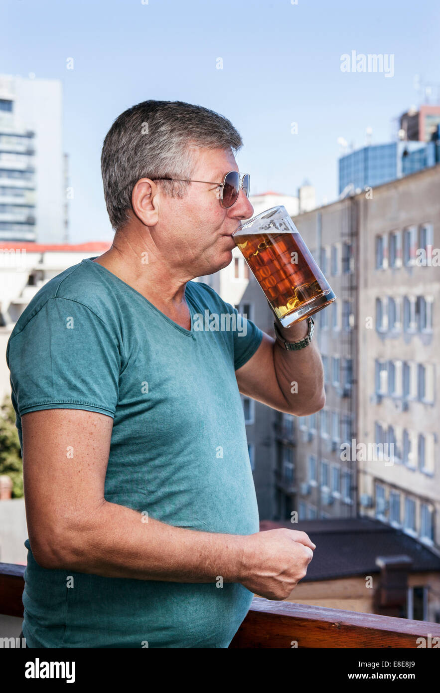 An older man drinks beer sipping it slowly overlooking an industrial landscape Stock Photo