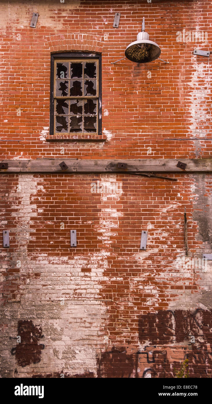 A broken multi pane window high up on a red brick wall. Stock Photo
