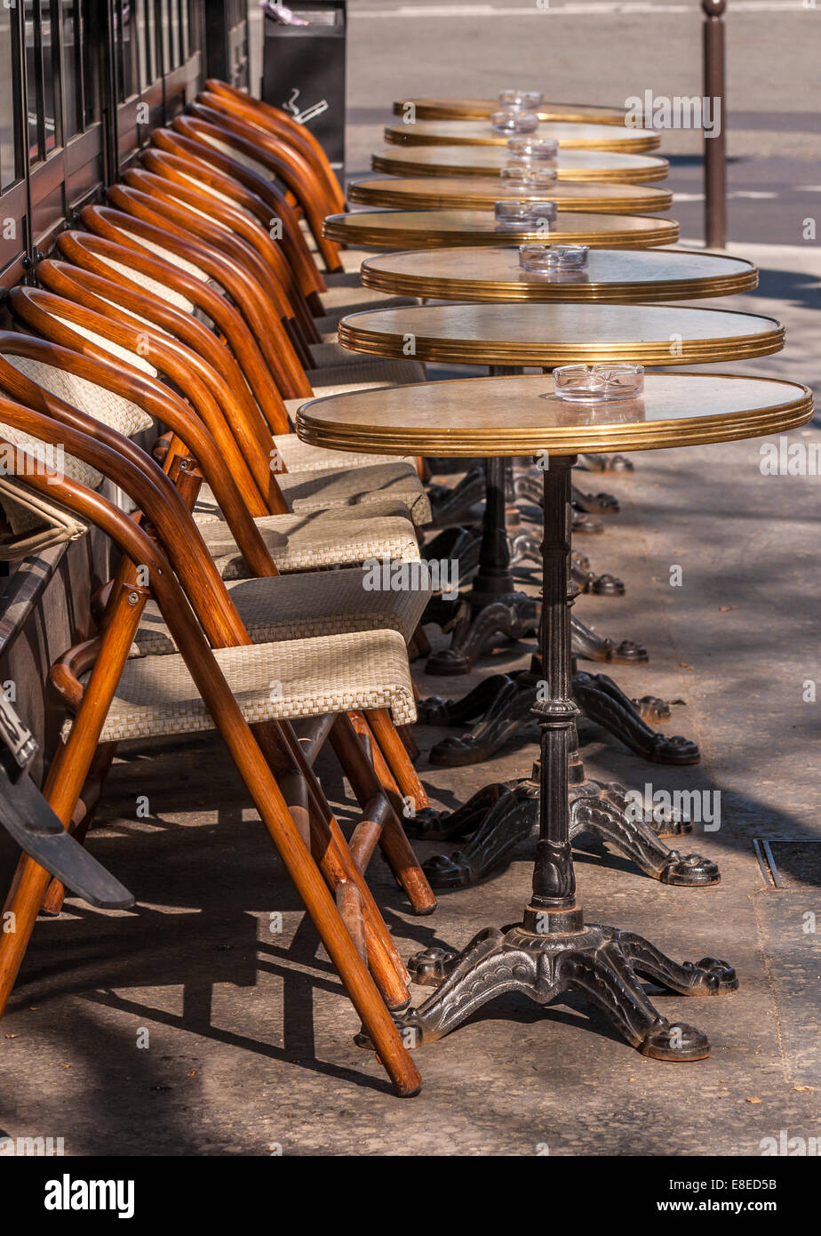 Bistro chairs and tables with ash trays sit empty in the sun. Stock Photo