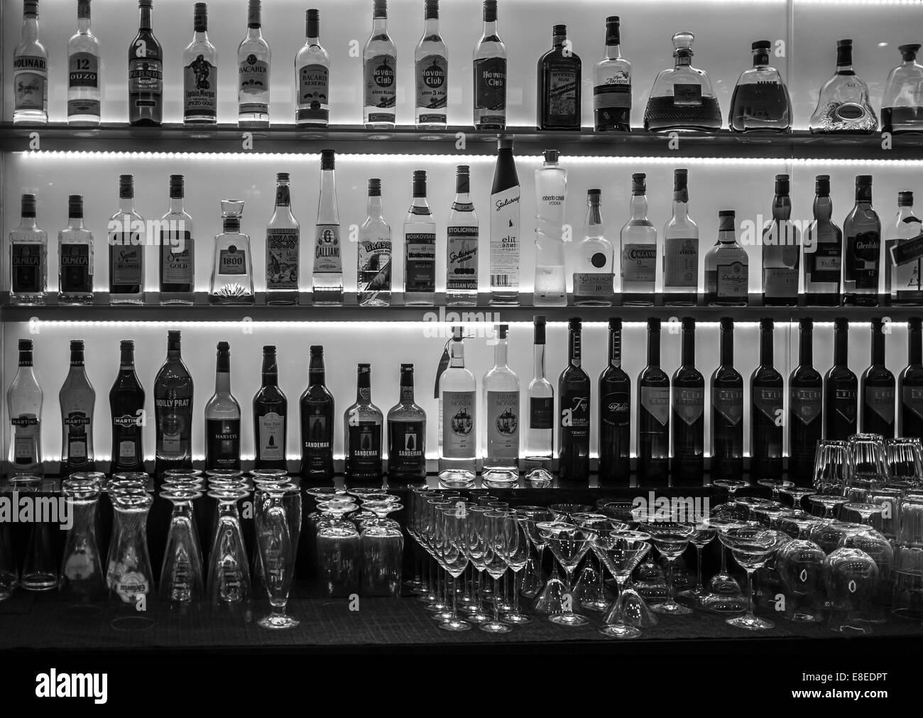 Bottles of wine, liquor and spirits as well as glasses on a back lit bar. Stock Photo