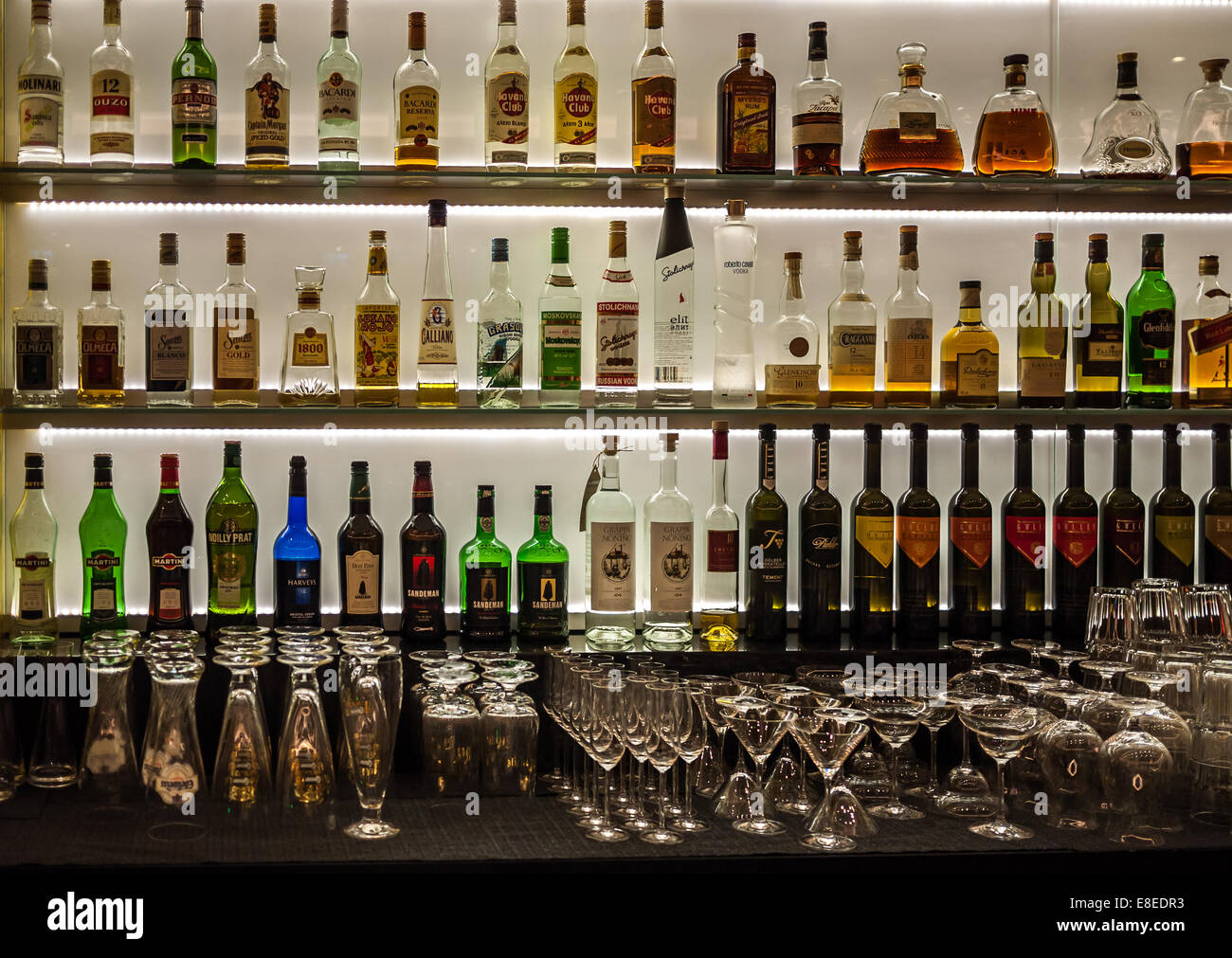 Bottles of wine, liquor and spirits as well as glasses on a back lit bar. Stock Photo