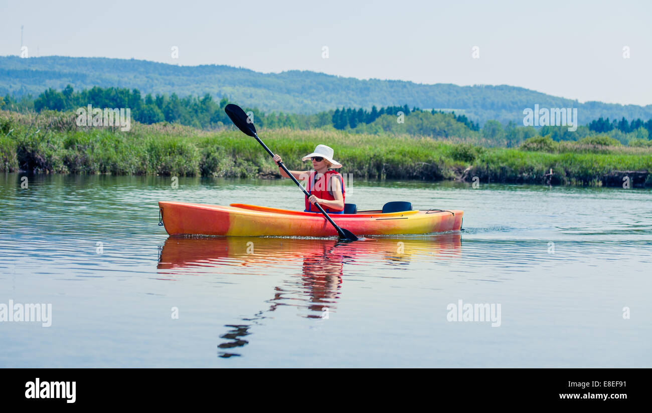 Young Woman Kayaking Alone on a Calm River and Wearing a Safety Vest
