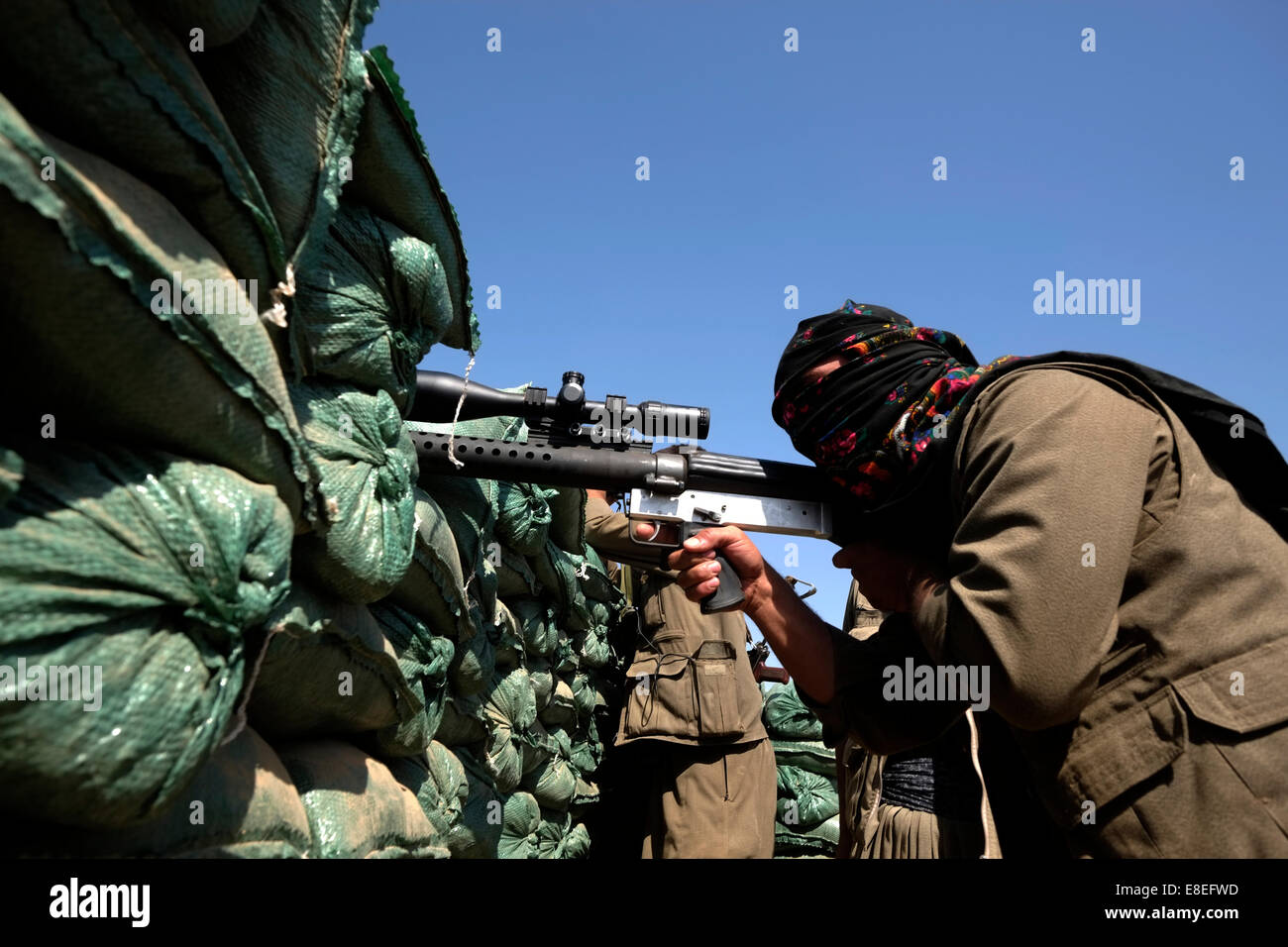 A Kurdish sniper of the People's Defense Forces HPG the military wing of the Kurdistan Workers' Party PKK firing from a front line outpost at ISIS or ISIL location in the village of Uzeira near the city of Kirkuk in northern Iraq Stock Photo