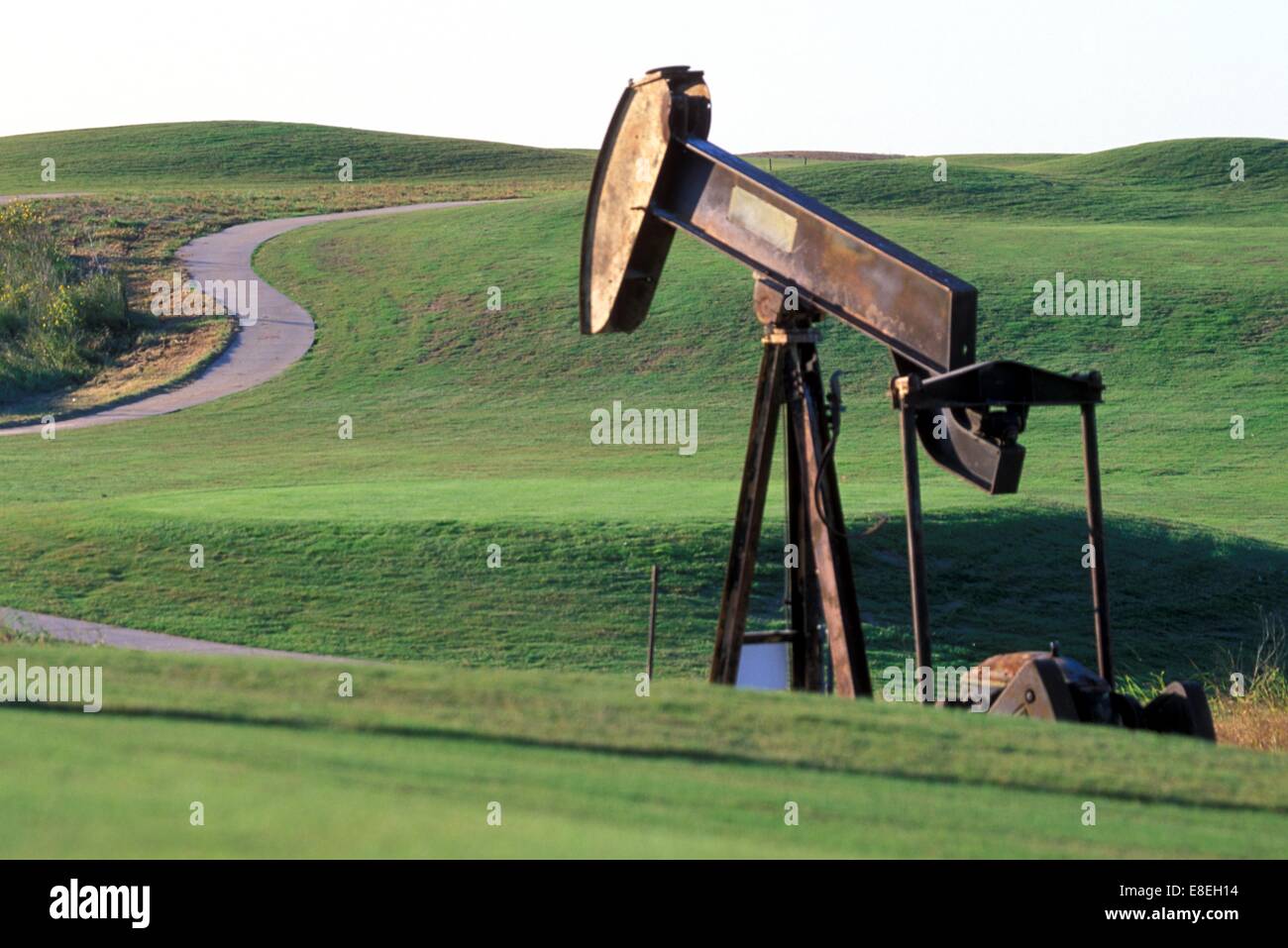 Pump Jack Operating Along Road in Green Hills Stock Photo Alamy