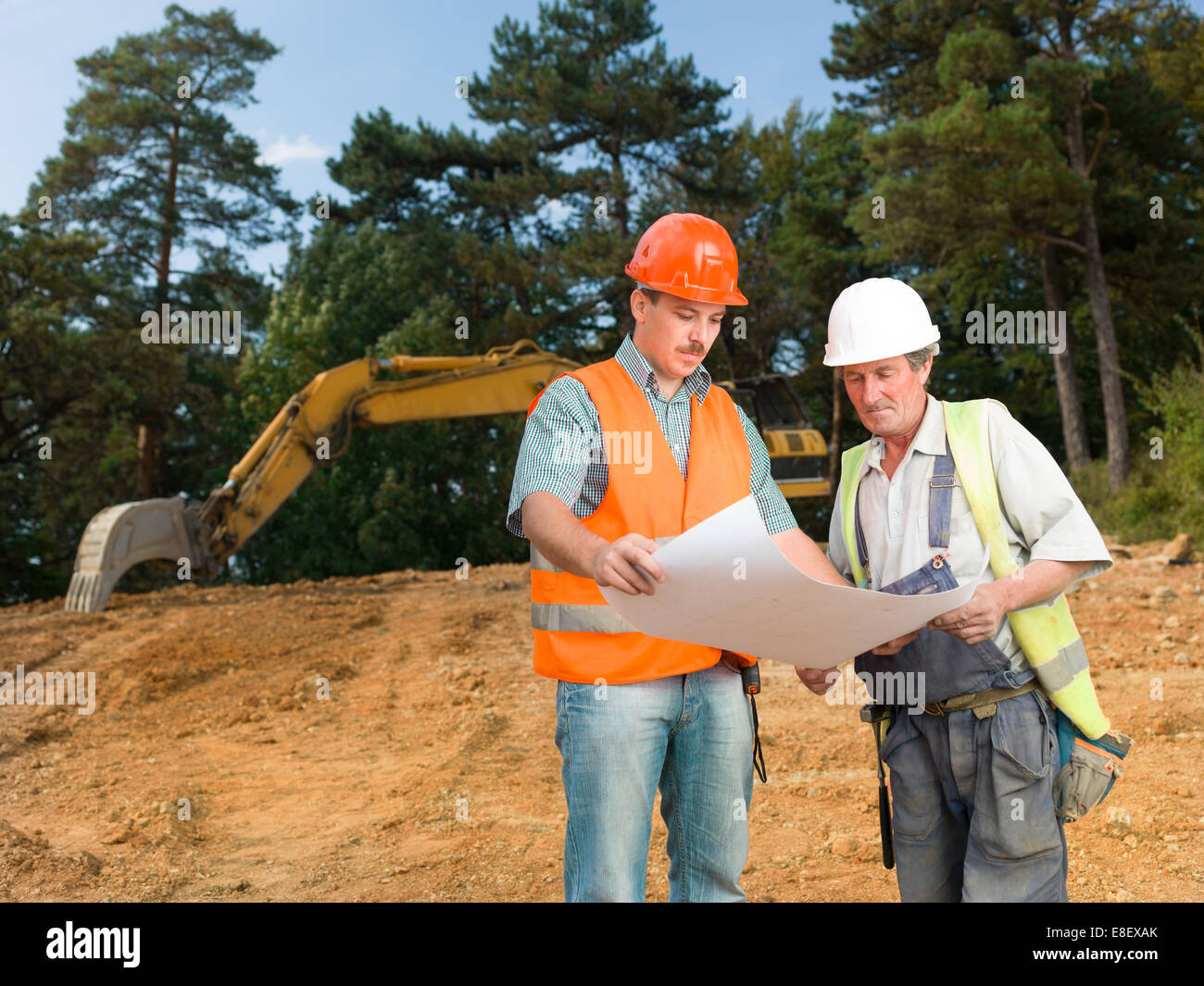 front view of manager and builder on construction site looking at blueprint and discussing it Stock Photo