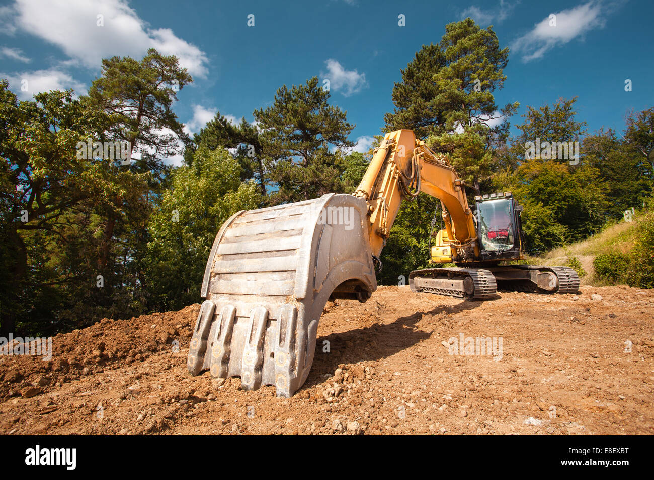 perspective view of excavator on new construction site with trees and blue sky in background Stock Photo