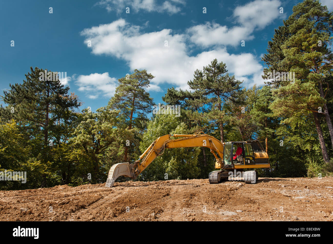 side view of excavator on new construction site with trees and blue sky in background Stock Photo