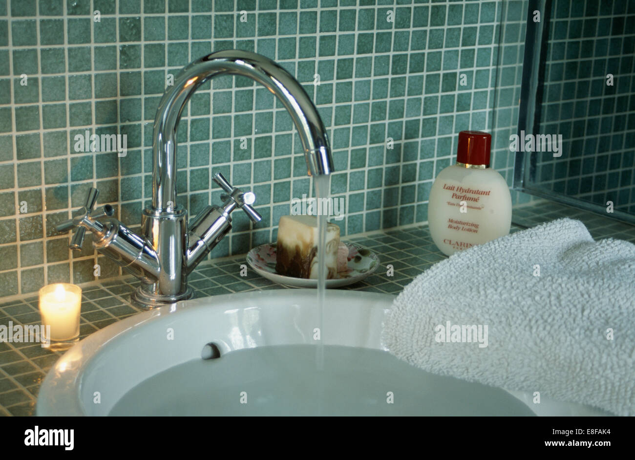 Close-up of lighted candle beside chrome tap pouring water into white basin  in mosaic tiled bathroom Stock Photo - Alamy