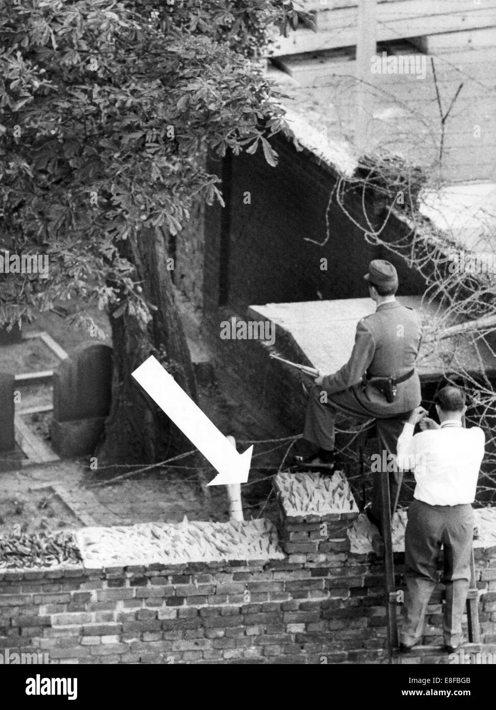 A West Berlin police officer viewing a spot behind the cemetery wall where the man broke down by shots. A 40 to 50 year old man got shot by East Berlin border guards during his escape attempt on the cemetery at the border corner Bernauer Street/ Berg Street on 4th September 1962. The Federal Republic of Germany and the German Democratic Republic were split into west and east by an iron curtain from 13th August 1961, the day of the building of Berlin Wall, to the fall of the wall on 9th November 1989. Stock Photo