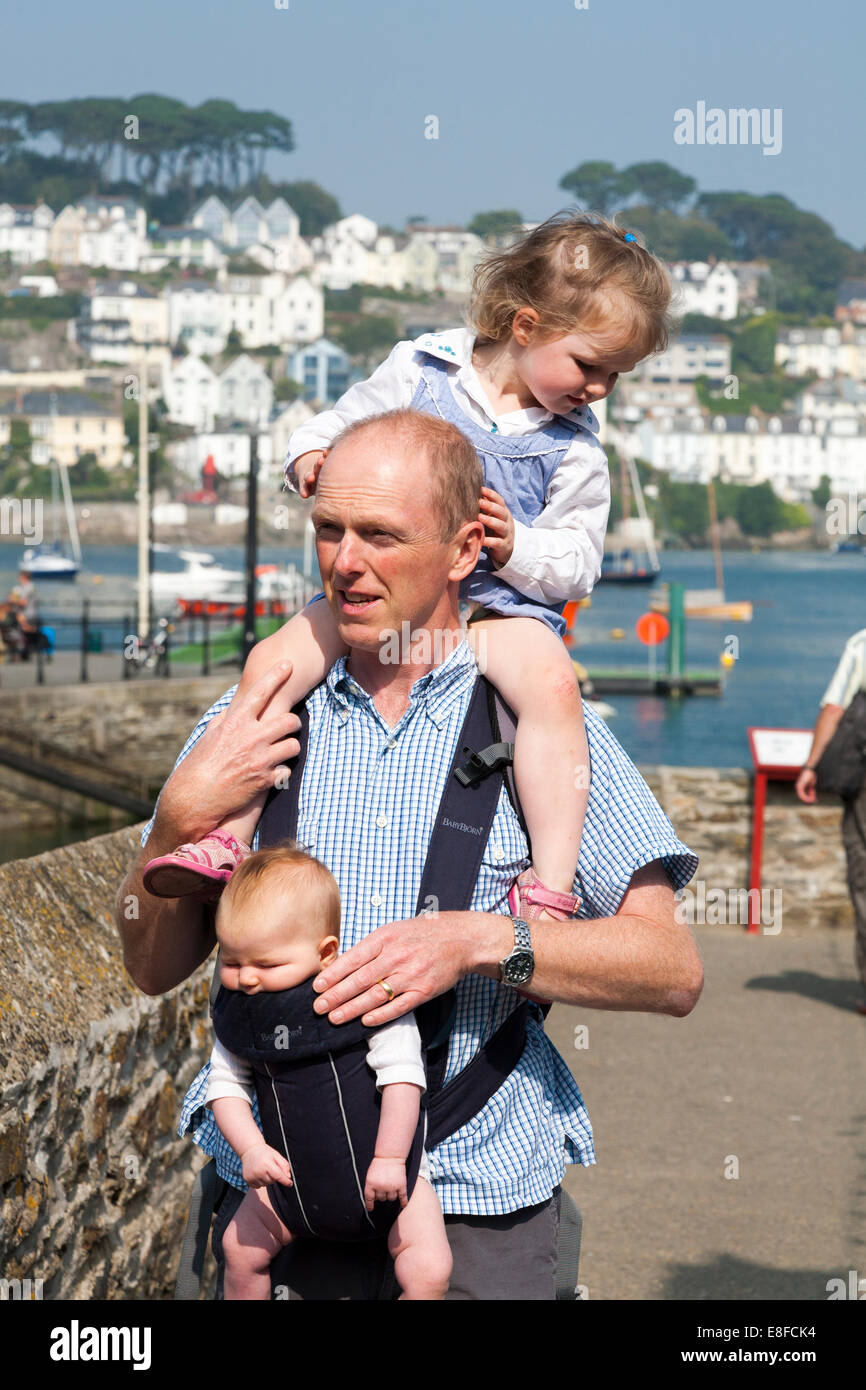 Mature dad / father with two / 2 children; one child on shoulders and baby In sling. Cornwall UK. Stock Photo