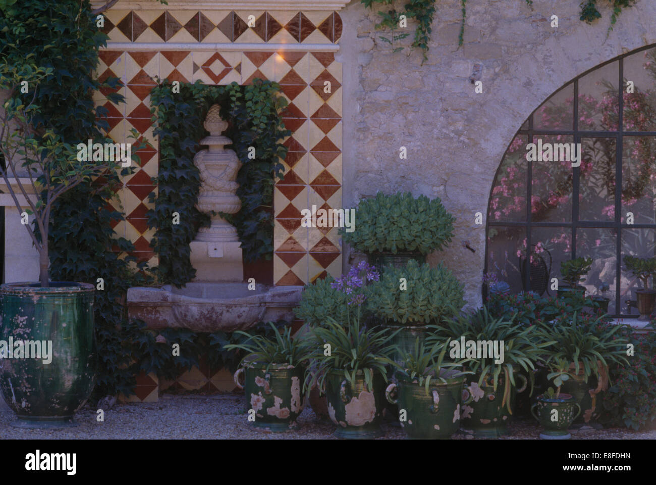 Tiled surround on alcove with stone urn in courtyard with green plants in glazed rustic pots Stock Photo