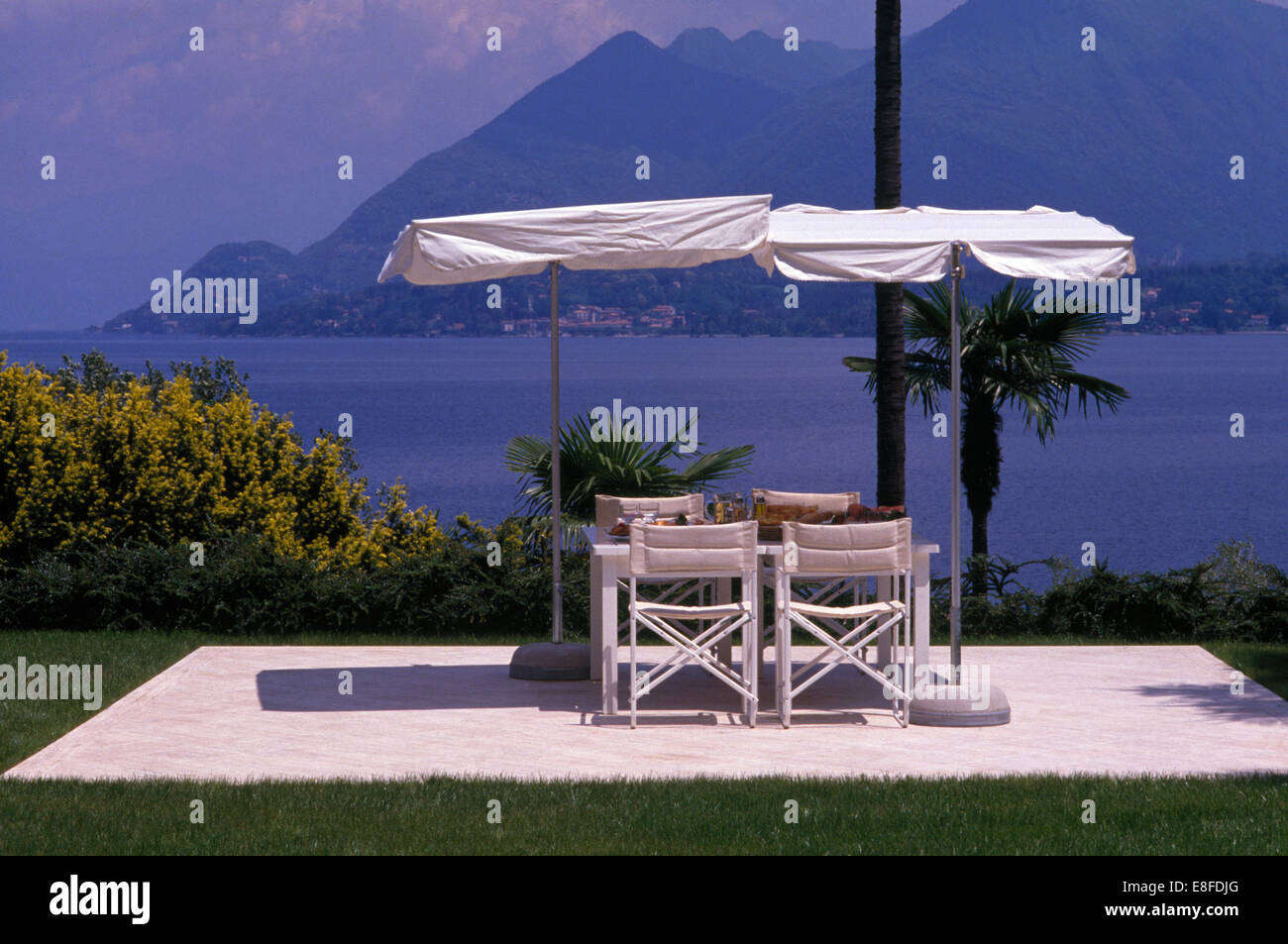 White umbrellas above white chairs and table on stone terrace overlooking the sea off the coast of Corsica Stock Photo