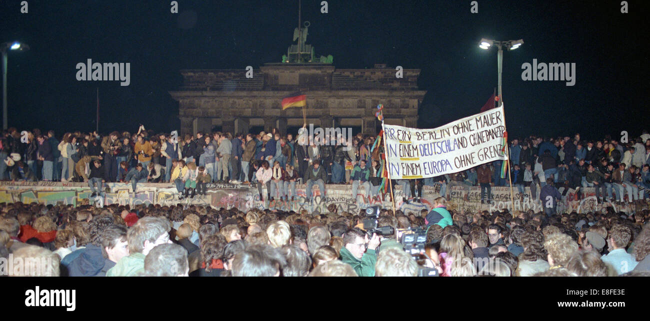 One day after the opening of the border, thousands of people celebrate on, in front of and behind Berlin Wall at Brandenburg Gate in Berlin on 10 November 1989 (western side). The inner-German border which had separated the country since 1961 practically ceased to exist. A poster in the foreground of the picture reads:'For a Berlin without a Wall in a Germany without tanks in a Europe without borders'. Photo: Peter Zimmermann Stock Photo