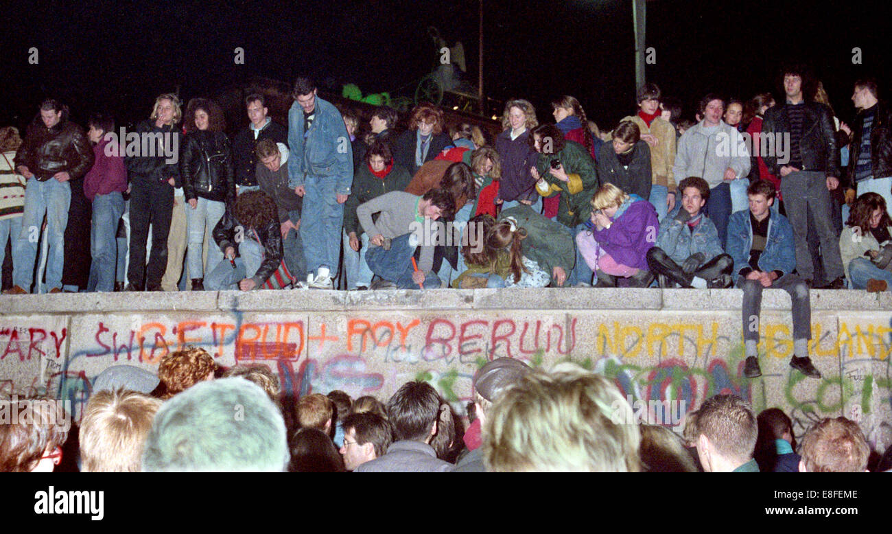 One day after the opening of the border, thousands of people celebrate on, in front of and behind Berlin Wall at Brandenburg Gate in Berlin on 10 November 1989 (western side). The inner-German border which had separated the country since 1961 practically ceased to exist. In the middle of the picture, young people are busy breaking small pieces out of the Wall which later on became popular souvenirs for tourists. Photo: Peter Zimmermann Stock Photo