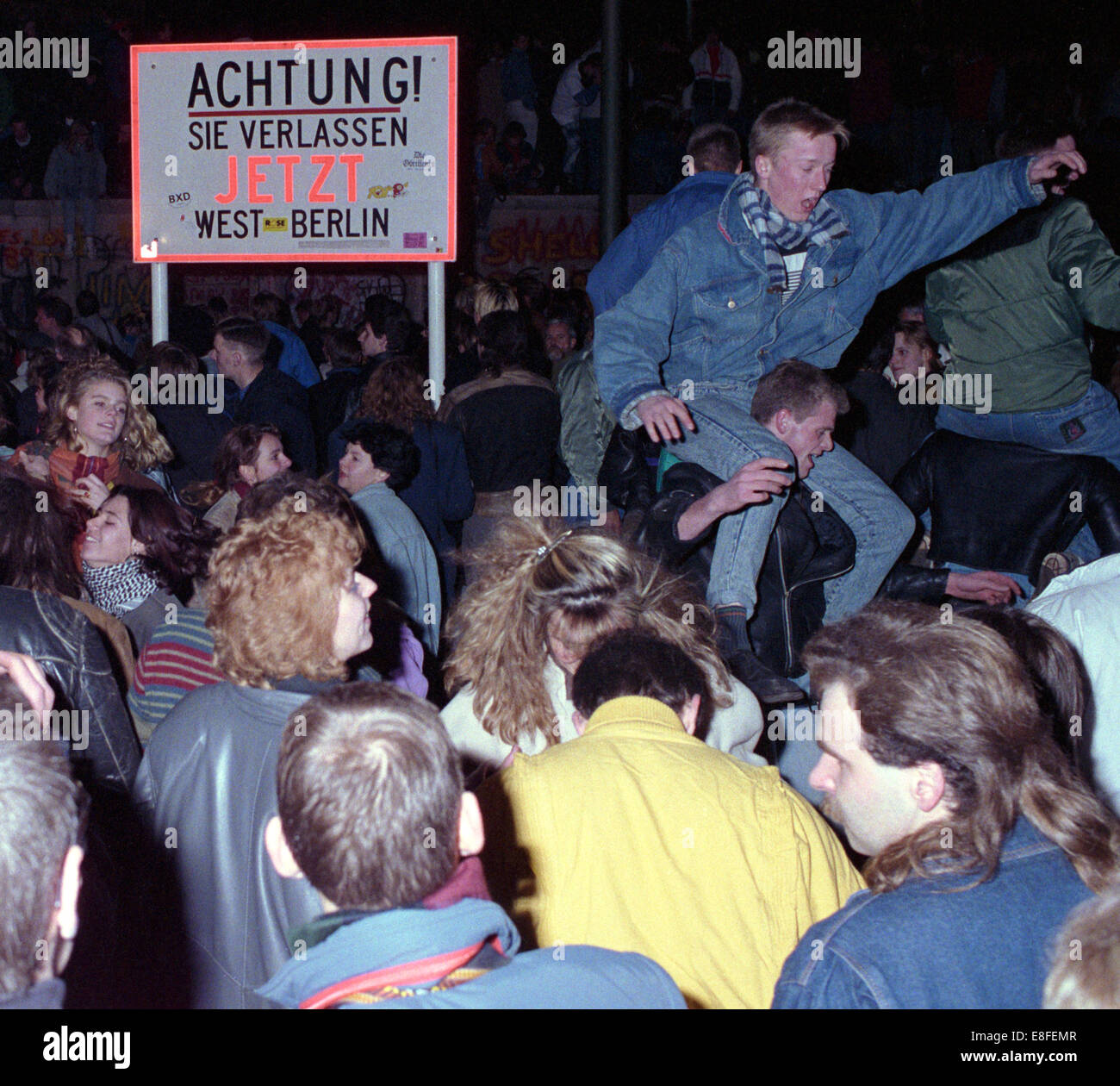 One day after the opening of the border, thousands of people celebrate on, in front of and behind Berlin Wall at Brandenburg Gate in Berlin on 10 November 1989 (western side). The inner-German border which had separated the country since 1961 practically ceased to exist.The sign in the picture reads 'Attention,you are leaving West-Berlin'. Photo: Peter Zimmermann Stock Photo