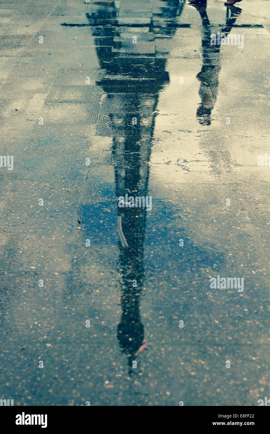 Reflection of man walking past Eiffel Tower in a puddle, Paris, France Stock Photo