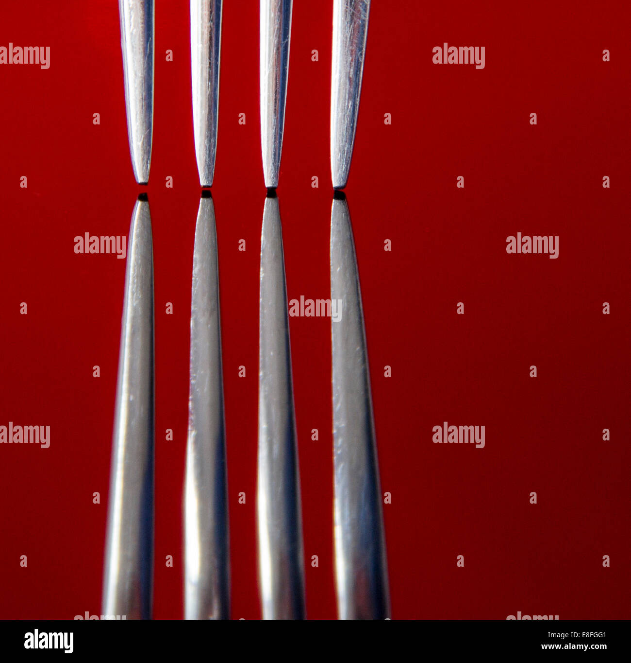 Close up of fork prongs on red reflective surface, studio shot Stock Photo