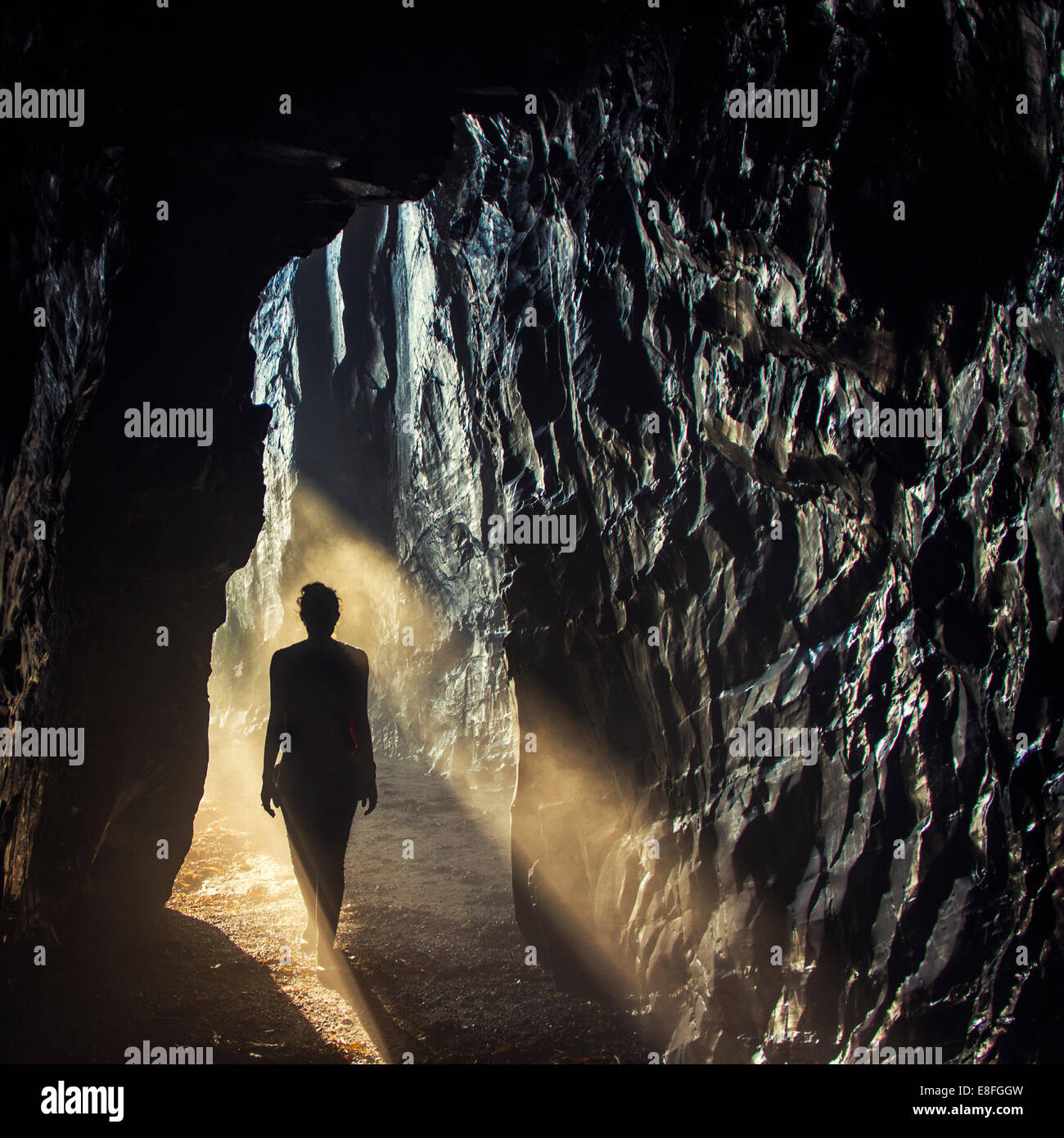 Silhouette of a woman walking into a cave Stock Photo