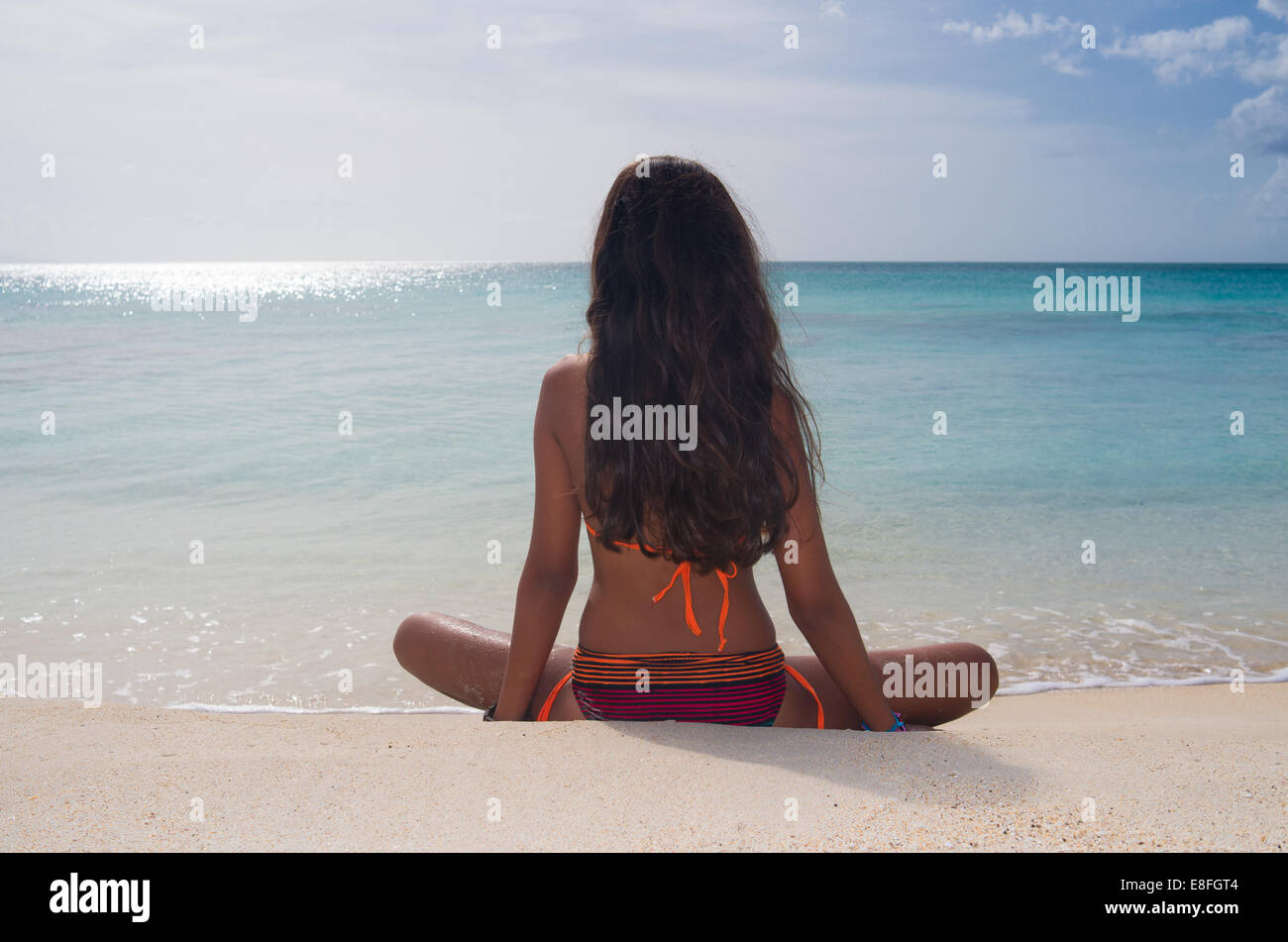 Rear view of girl sitting on Darkwood beach, Antigua, Caribbean Stock Photo