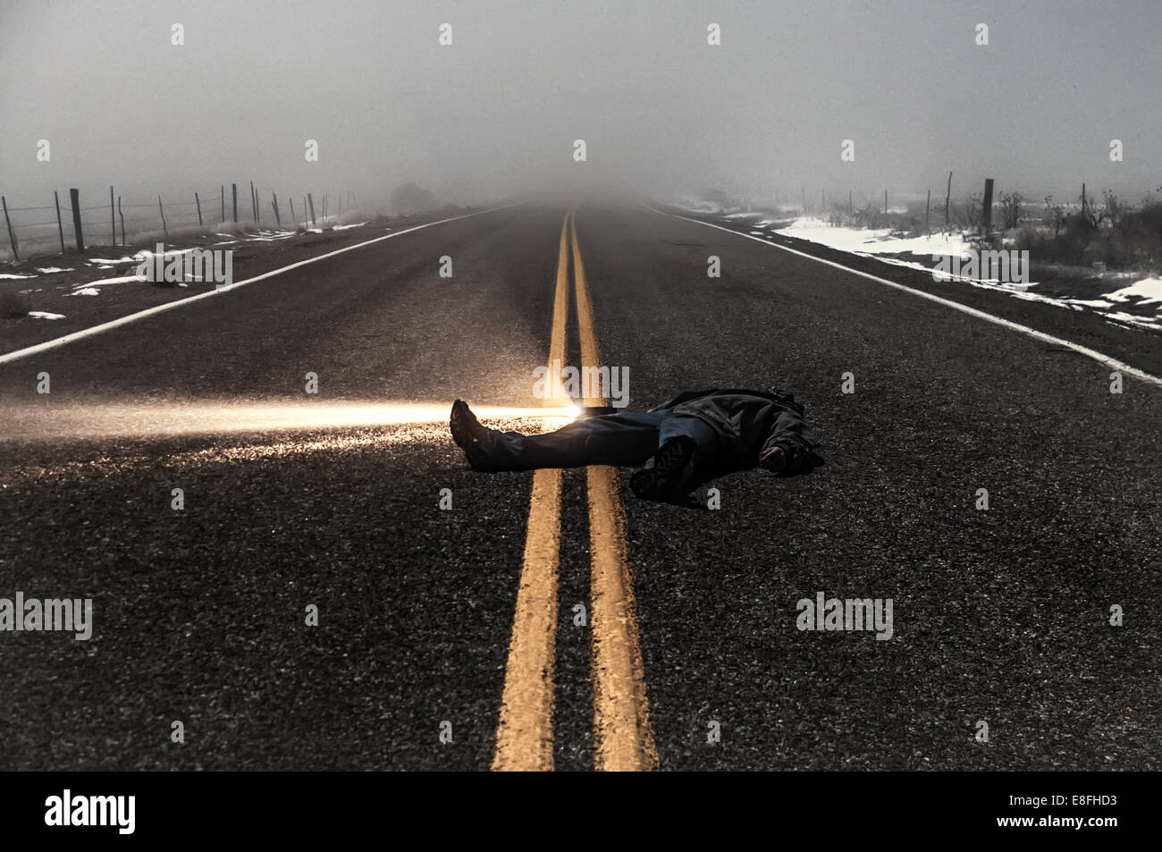 Man with flashlight lying in the middle of the road in fog, Idaho, USA Stock Photo