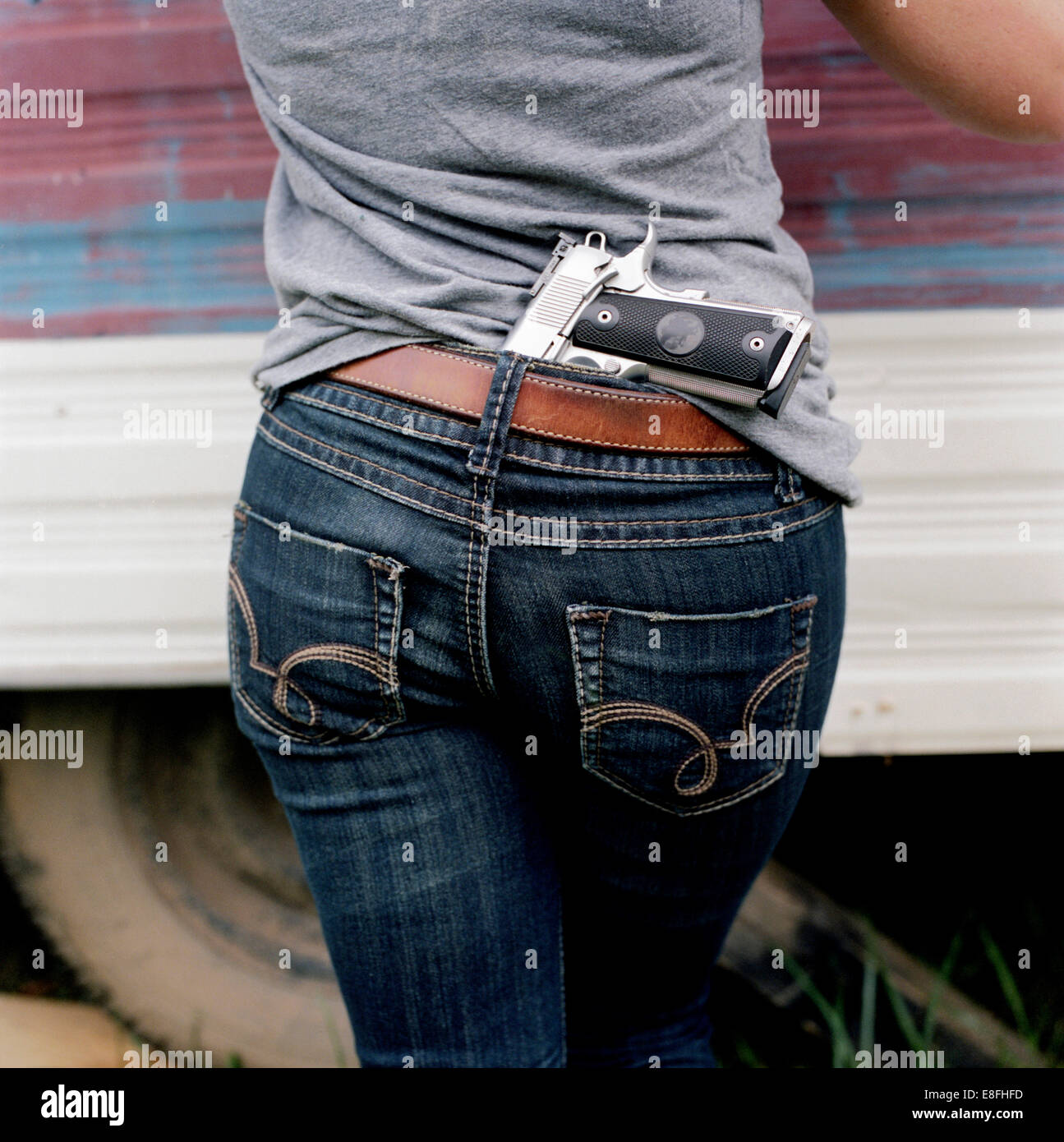 Woman with a handgun tucked into the back of her jeans Stock Photo