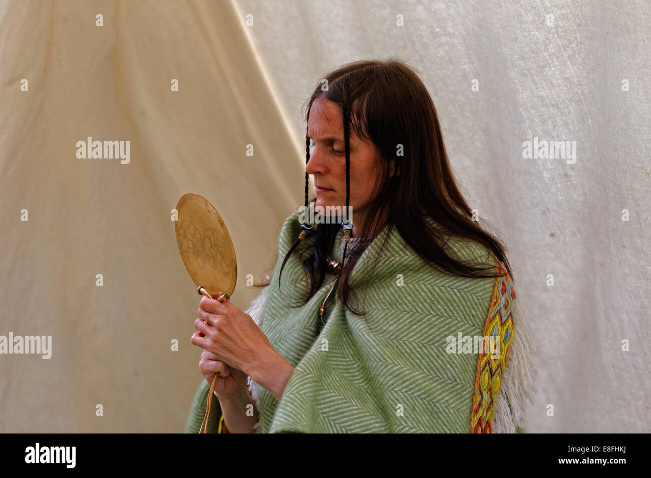 Woman dressed as a  Briton looks into a polished copper alloy mirror decorated similarly to the Trelan Bahow / St Keverne mirror Stock Photo