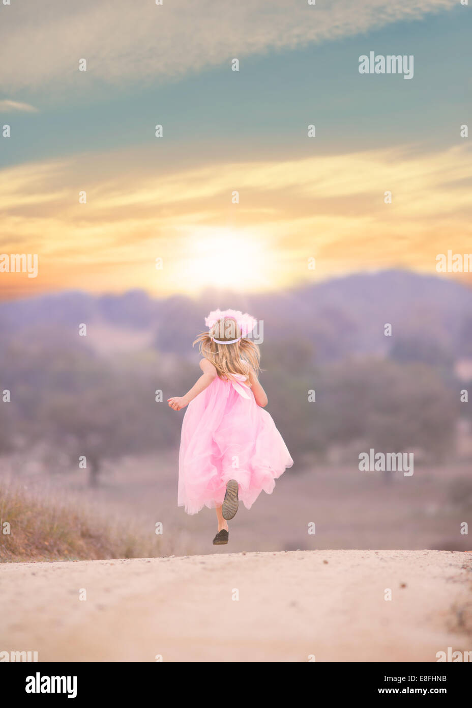 Girl wearing pink dress running down road Stock Photo