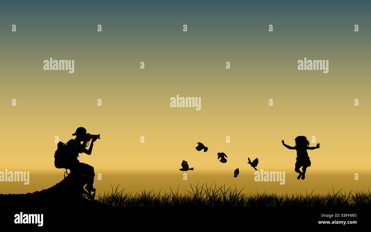 Silhouette of a photographer taking a photo of a girl jumping in air next to flying birds, Indonesia Stock Photo