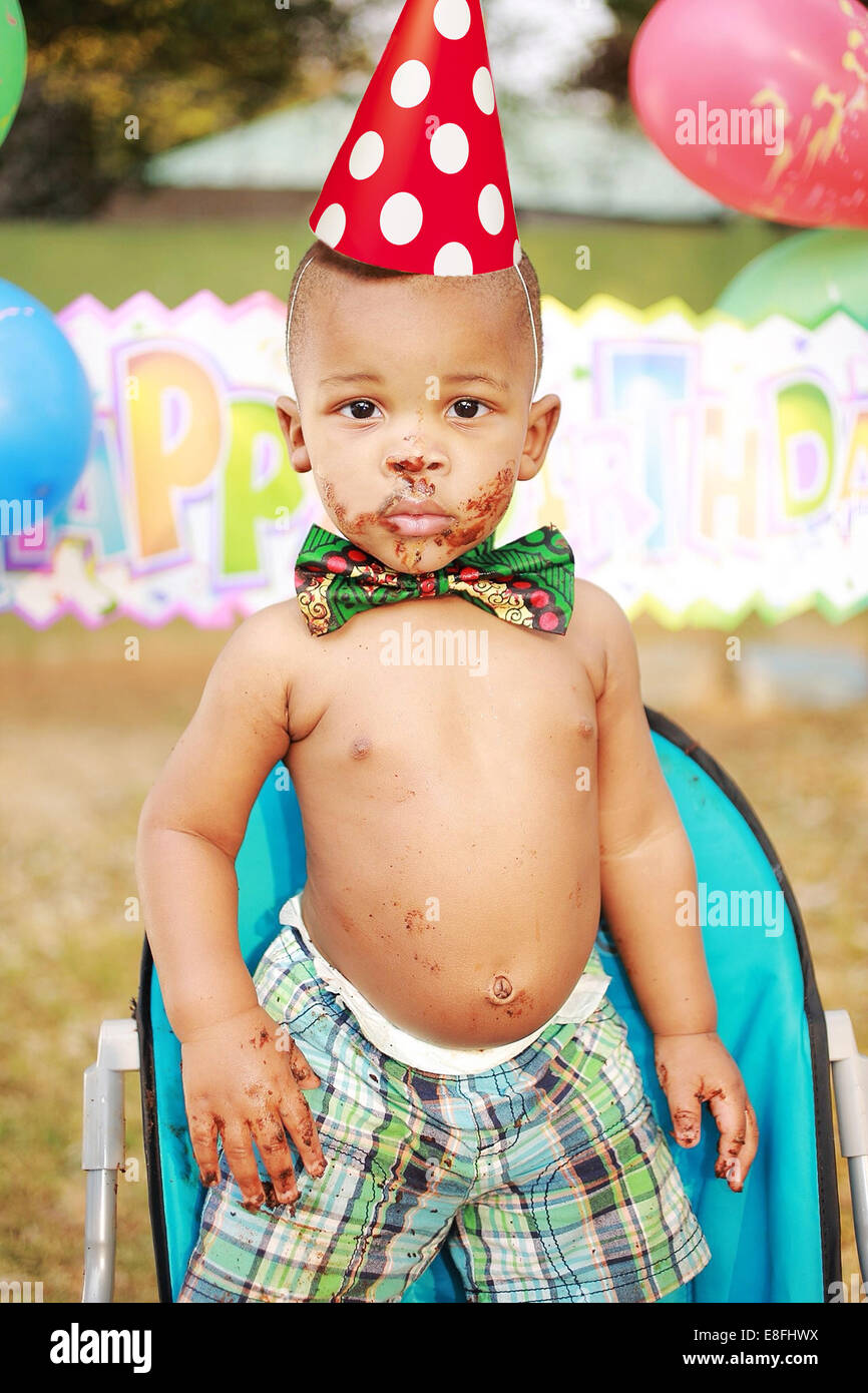 Portrait of a shirtless Boy at a birthday party with chocolate cake on his face and hands Stock Photo