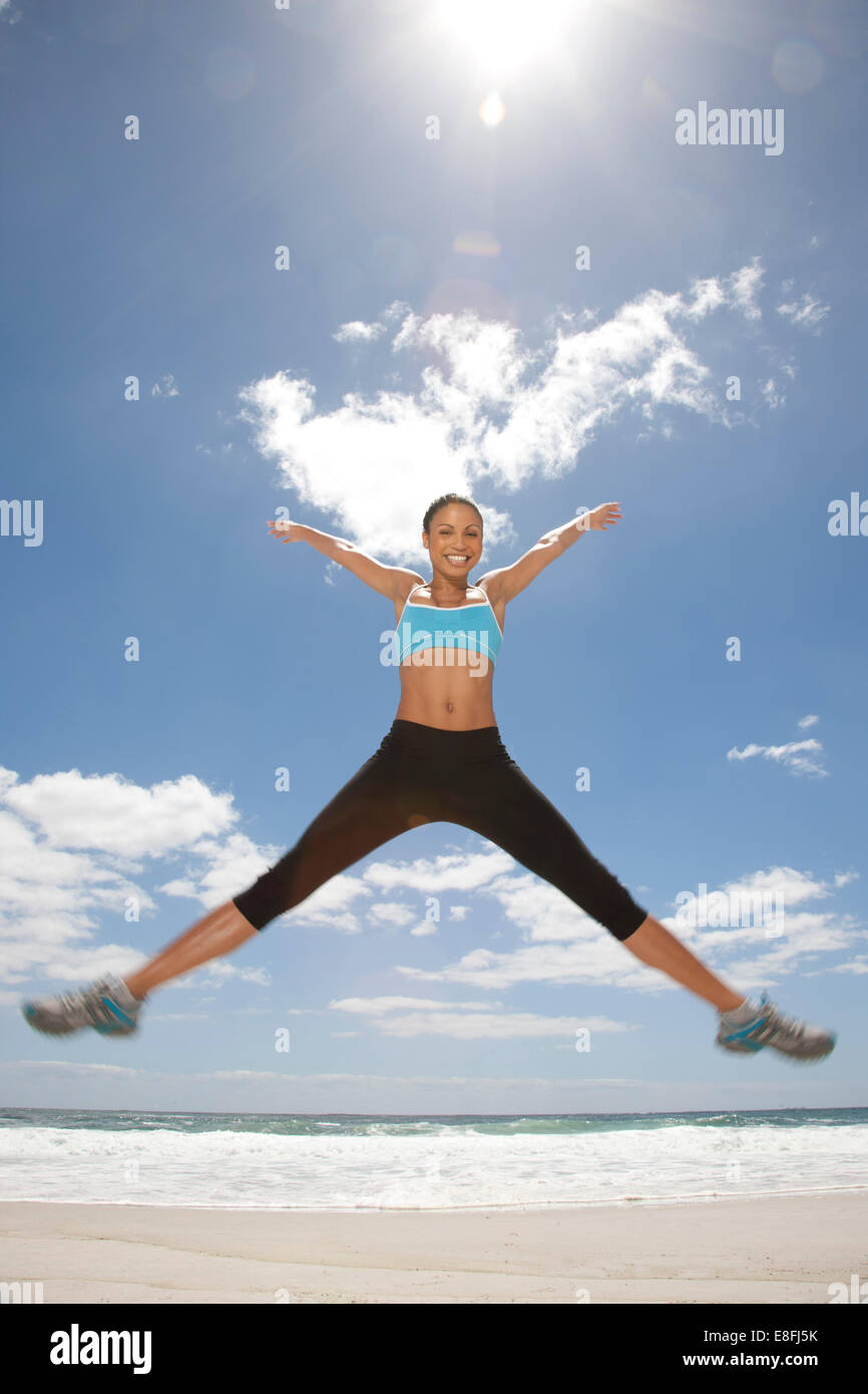 Smiling woman doing star jumps on beach, Cape Town, Western Cape, South Africa Stock Photo