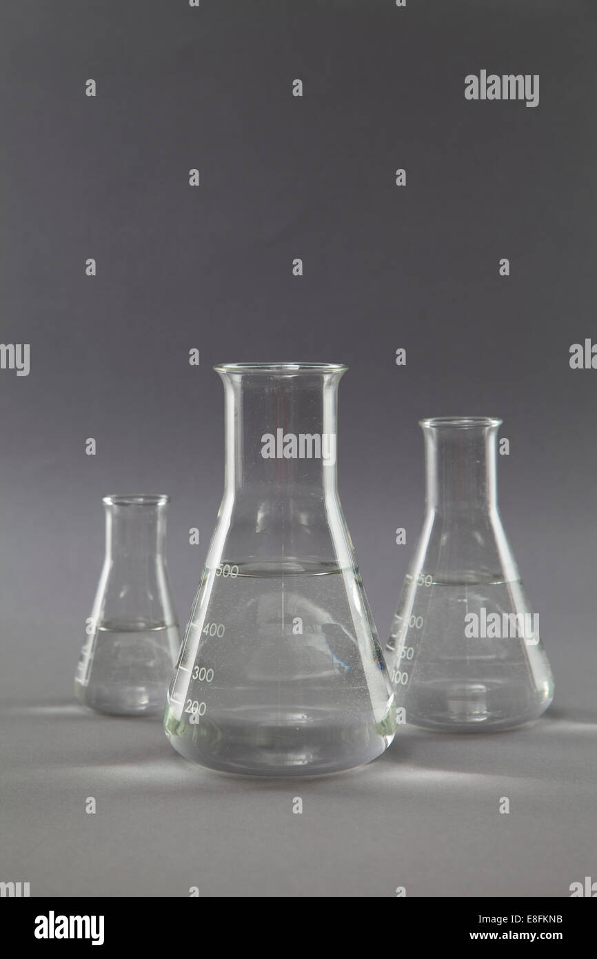 Three conical flasks and measuring beakers filled with clear liquid in