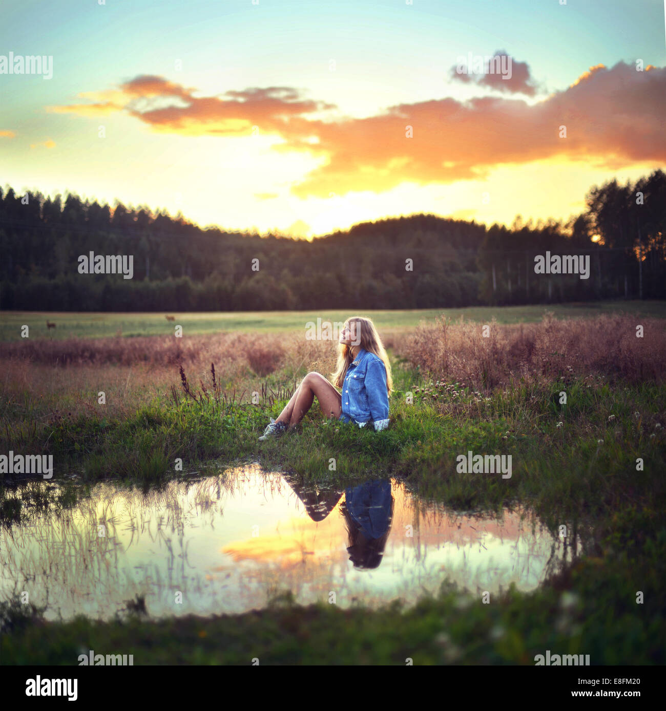 Woman sitting by a small pond at sunset, Norway Stock Photo - Alamy