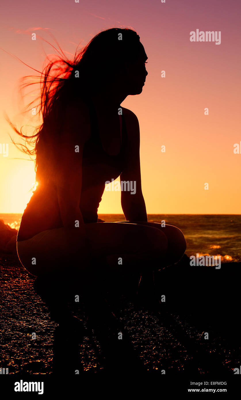 Silhouette of woman practising yoga on the beach at sunset Stock Photo