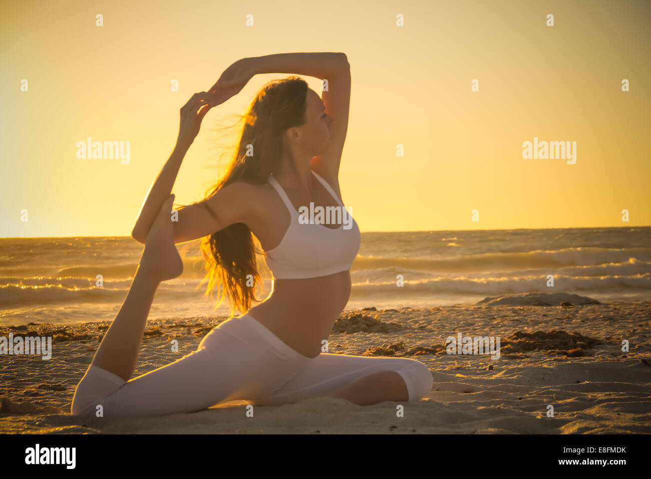 Woman practicing yoga on beach at sunrise Stock Photo