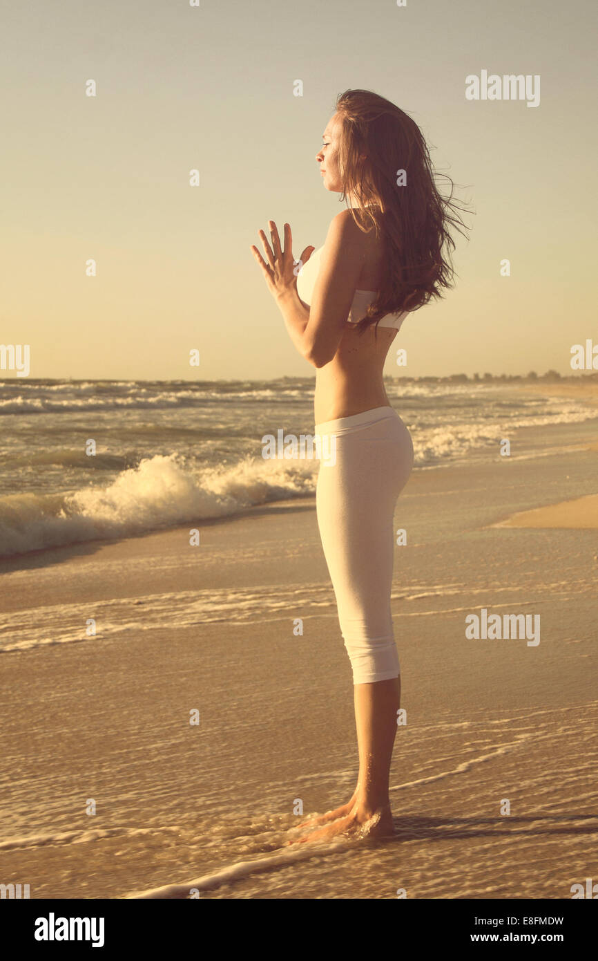 Side view of woman standing on beach doing yoga with hands in prayer position Stock Photo