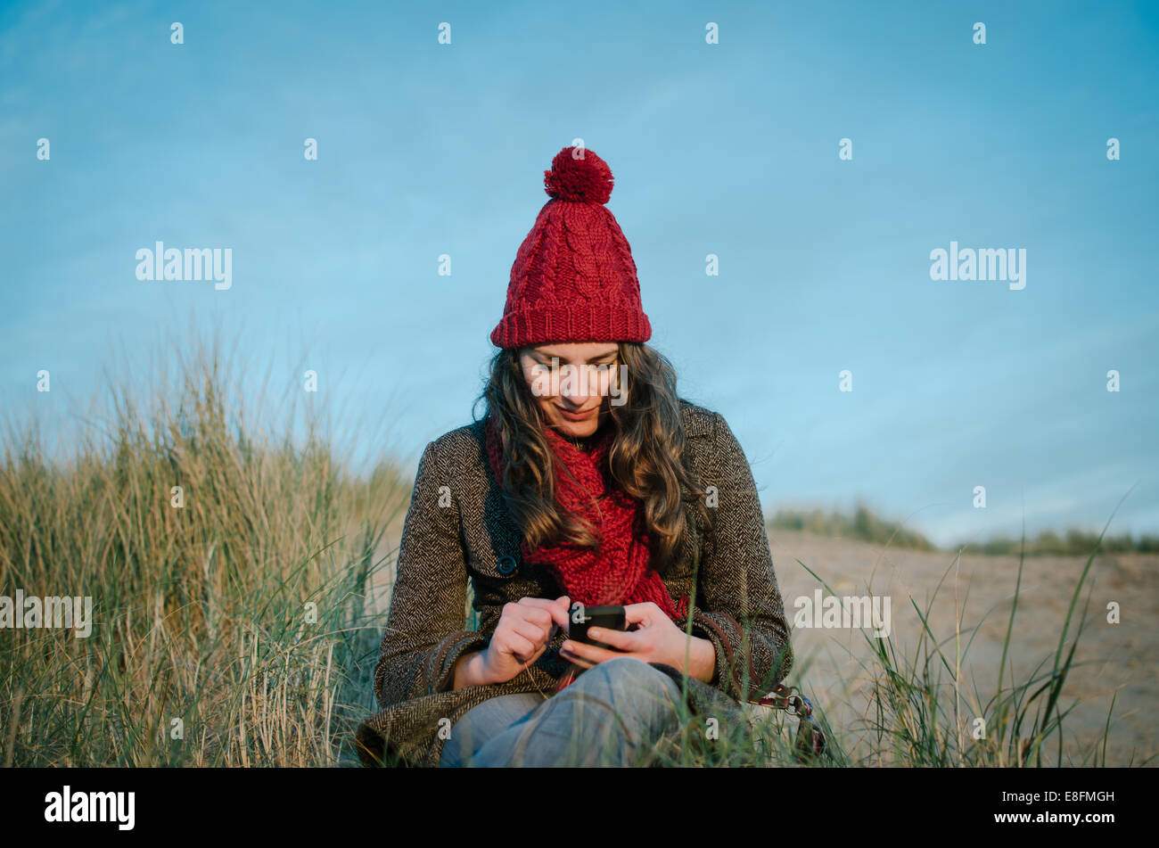 Woman sitting on beach texting, Netherlands Stock Photo