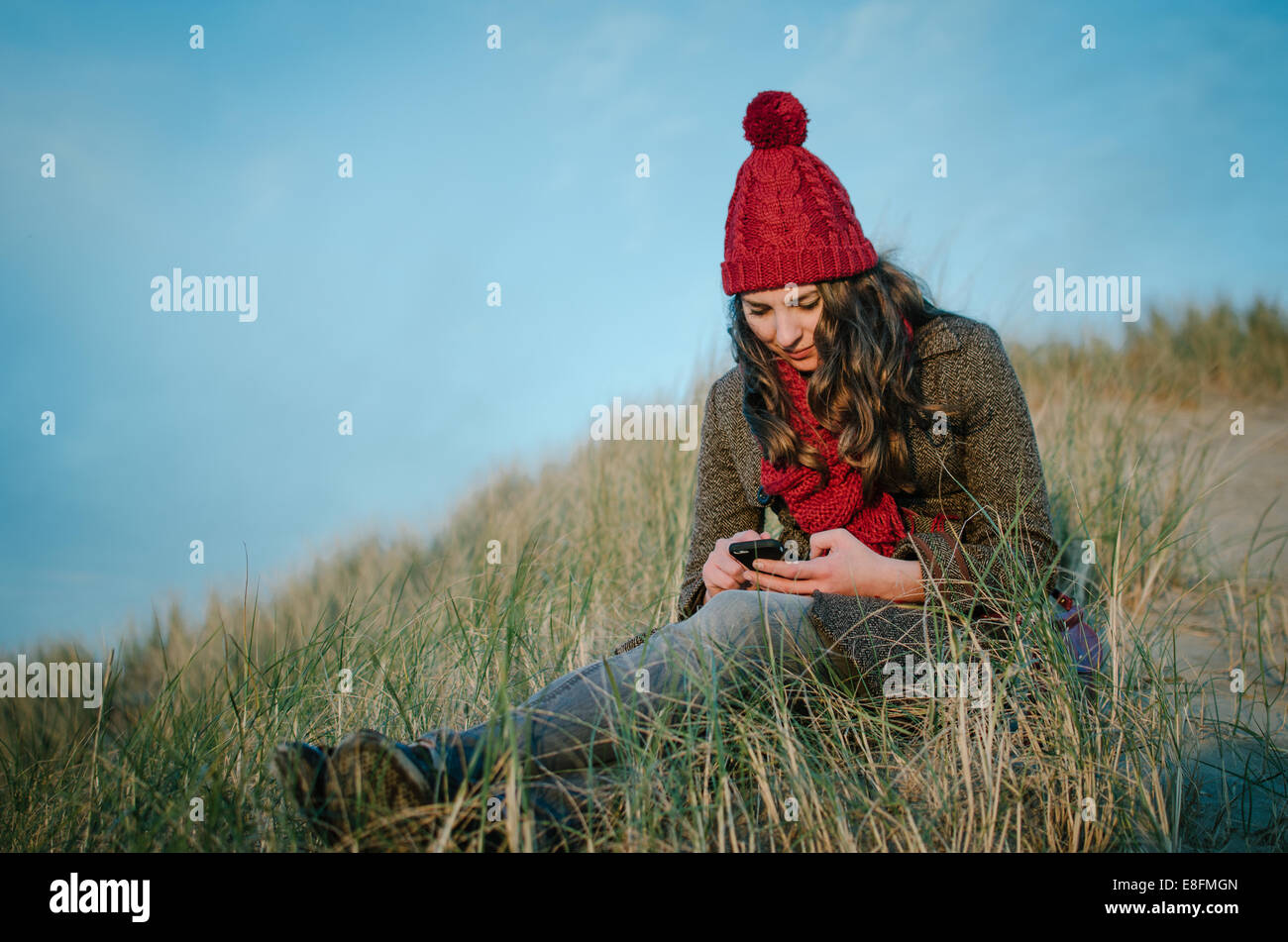 Woman sitting on beach texting, Netherlands Stock Photo
